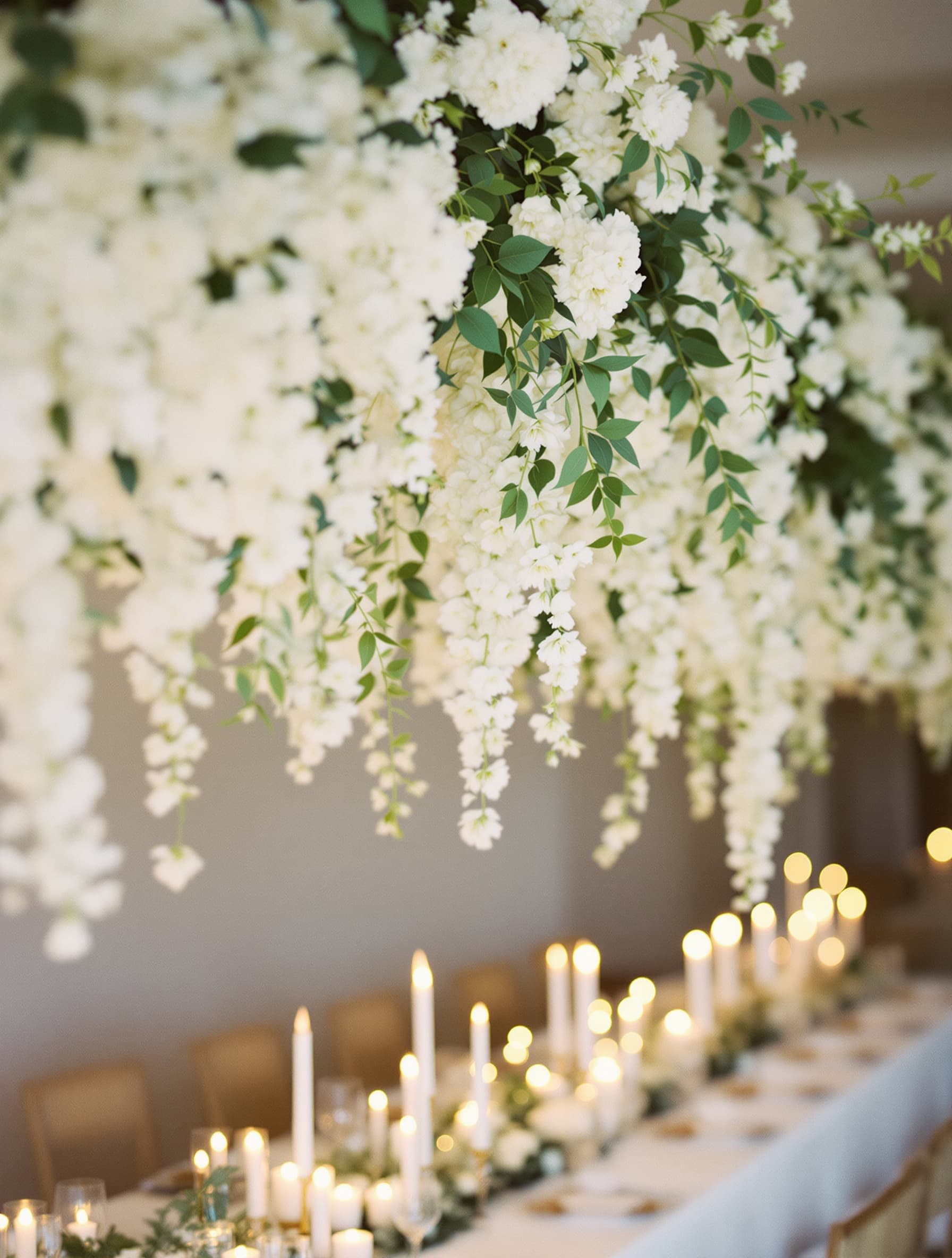Floral installation hanging above a long reception table set for a wedding with candles