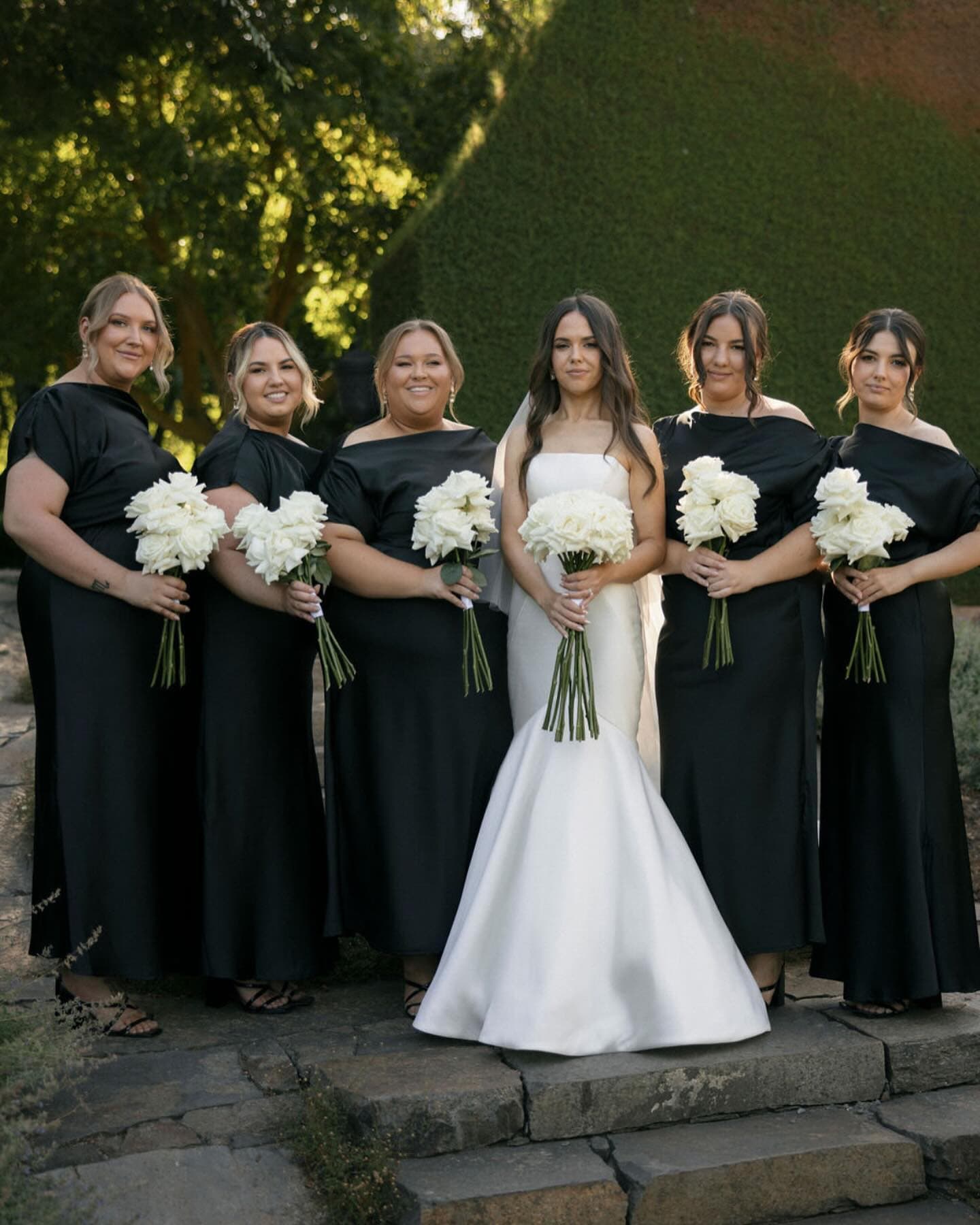 Bride with five bridesmaids and flower girl, all holding long-stem white rose bouquets