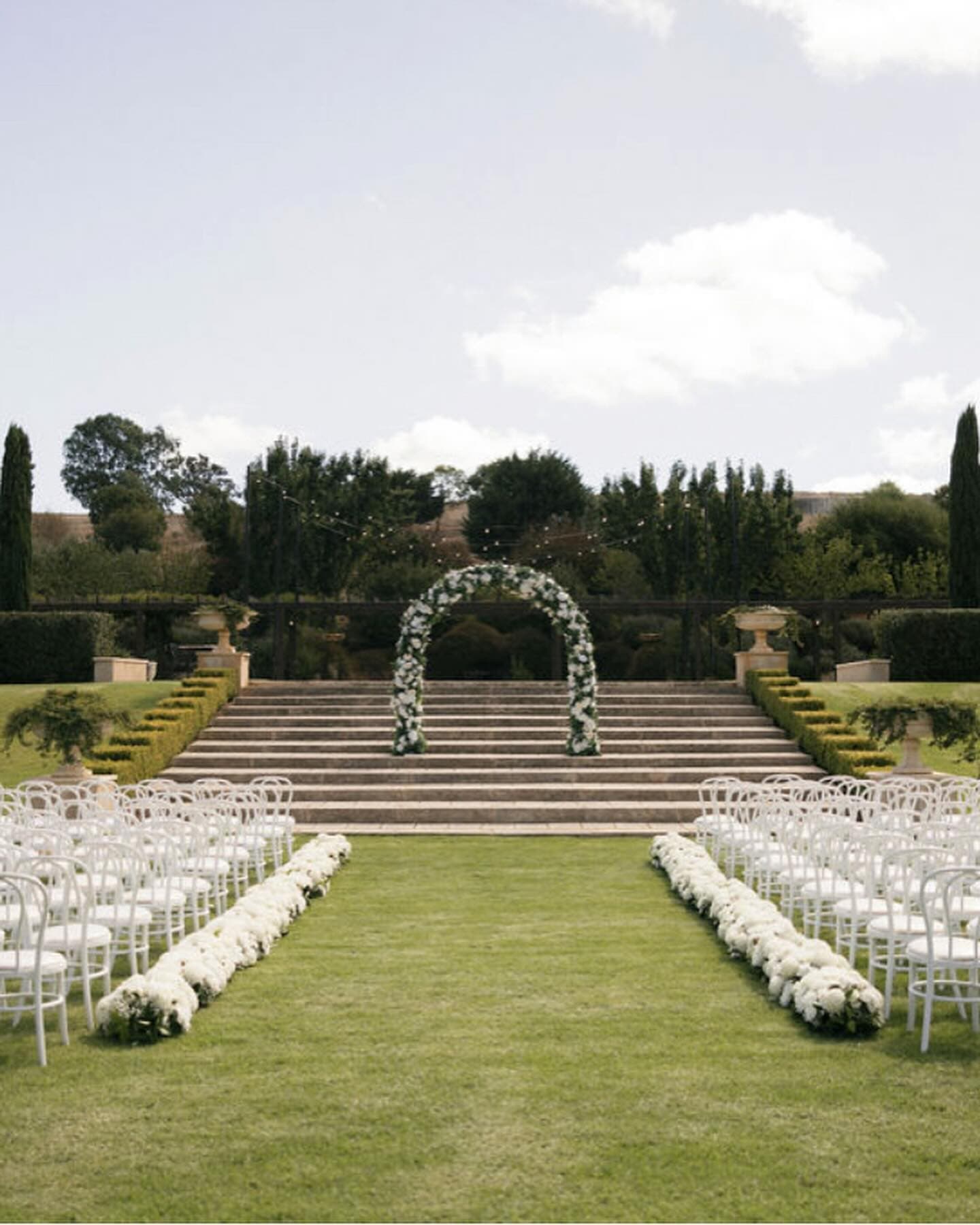 Garden ceremony aisle lined with a continuous white flower hedge installation at Mandalay House and Garden